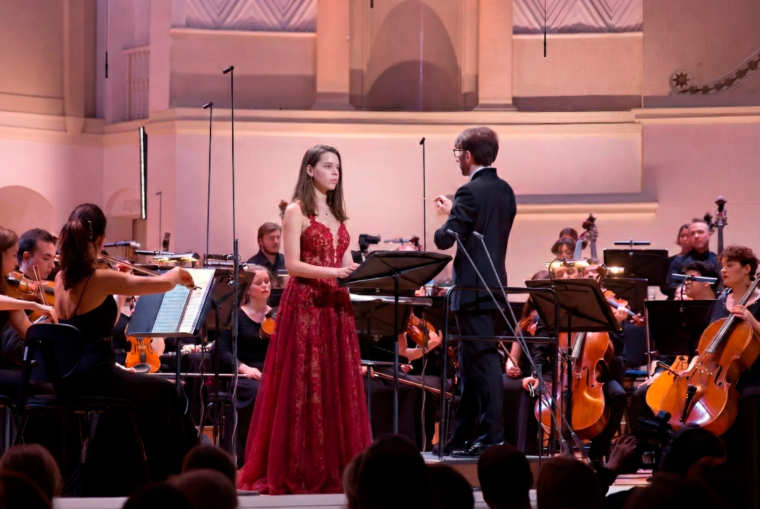 Yulia Pavlishcheva actúa con un vestido rojo junto a un director y una orquesta.